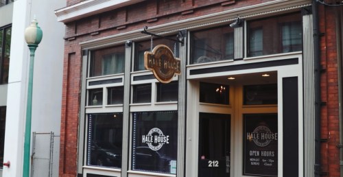 Exterior of Hale House, featuring a sign and large windows, with a brick building backdrop. Open hours displayed.