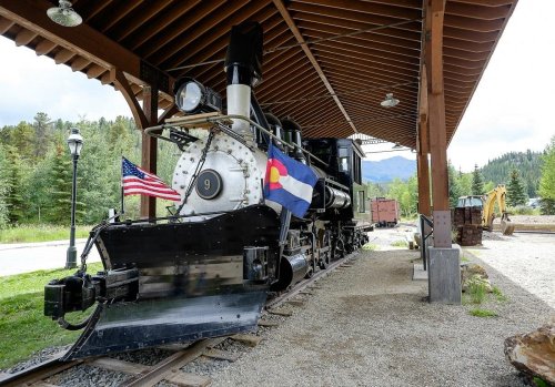 A vintage steam locomotive displayed under a wooden shelter, featuring American and Colorado flags.