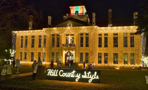 A beautifully lit historic building adorned with holiday lights, featuring a sign that reads "Hill County style."