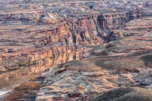 A scenic view of a canyon with a river and a bridge, showcasing layered rock formations and natural beauty.