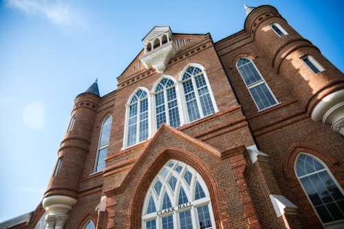 A close-up view of Clark Hall, showcasing its brick facade and large arched windows against a clear blue sky.