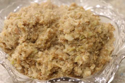 A close-up of a textured, beige mixture in a clear glass bowl, resembling a thick, grainy paste.