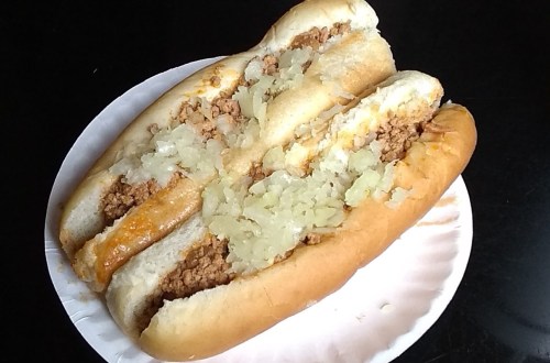 Three hot dogs topped with ground meat and chopped onions on a paper plate.