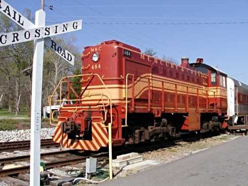 A vintage red and yellow train engine at a railroad crossing sign, with a passenger car attached.