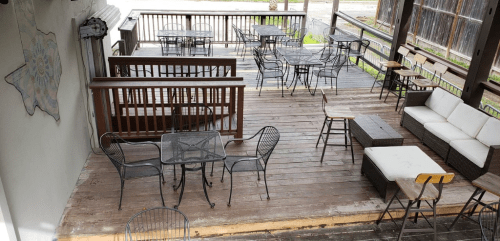 A spacious outdoor deck with wooden flooring, featuring various tables and seating arrangements.