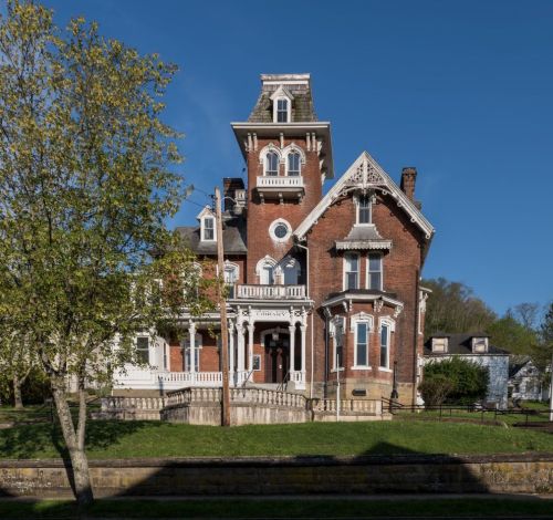A large, ornate Victorian mansion with a tower, surrounded by green grass and trees under a clear blue sky.