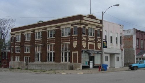 Historic brick building with large windows, labeled "First National Bank," set in a small town with cloudy skies.