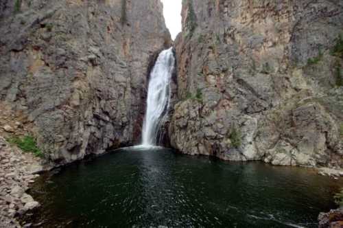 A waterfall cascades down rocky cliffs into a serene, dark green pool below.