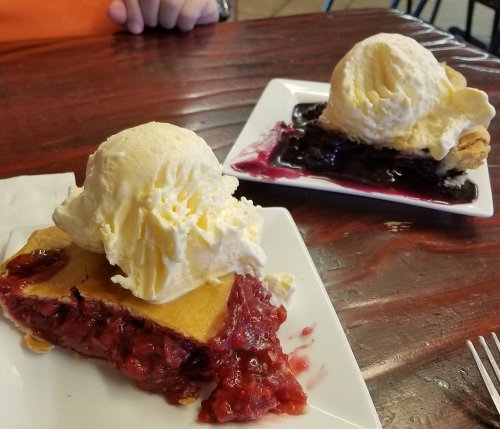 Two slices of pie topped with scoops of vanilla ice cream, one with cherry filling and the other with blueberry filling.