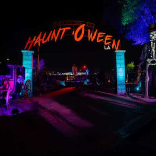 A spooky Halloween display with colorful lights, skeletons, and a sign reading "Haunt-O-Ween LA" at night.