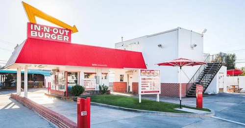 Exterior of an In-N-Out Burger restaurant featuring a red roof, menu board, and outdoor seating area.