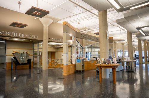 Interior of a library featuring modern architecture, display tables, and signage for various authors. Bright and spacious.