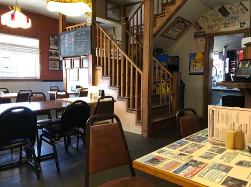 Cozy restaurant interior with wooden stairs, tables, and walls adorned with photos and menus.