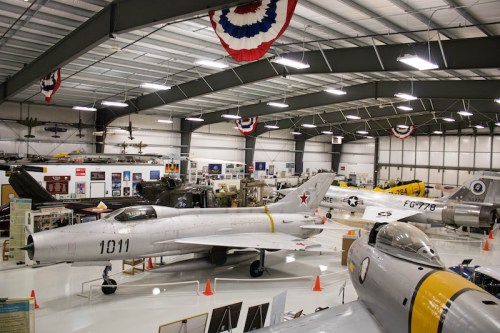 A spacious aircraft museum featuring various vintage planes and military memorabilia, decorated with patriotic banners.