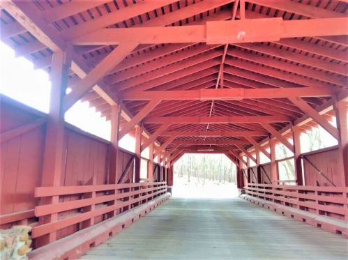 Interior view of a red covered bridge, showcasing wooden beams and a clear pathway leading to the exit.