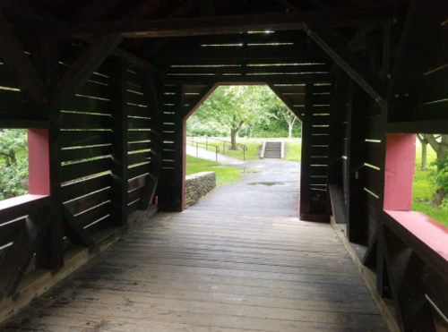 View from inside a covered bridge, looking out towards a path and greenery beyond.