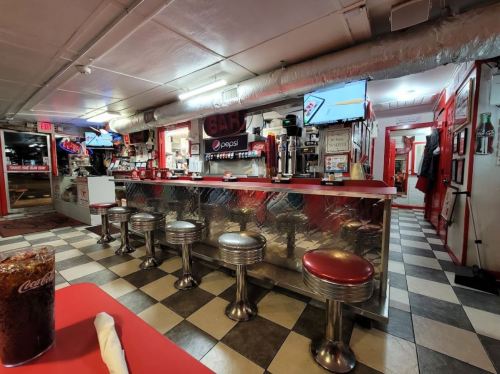 A retro diner interior featuring a red and silver bar, stools, checkered floor, and vintage decor.