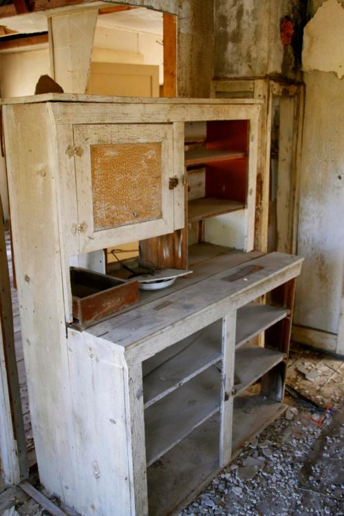 An old, weathered wooden cabinet stands in a dilapidated room, surrounded by debris and peeling walls.