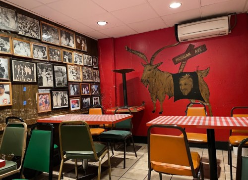 Cozy restaurant interior with checkered tables, colorful chairs, and a wall adorned with black-and-white photos and a goat mural.