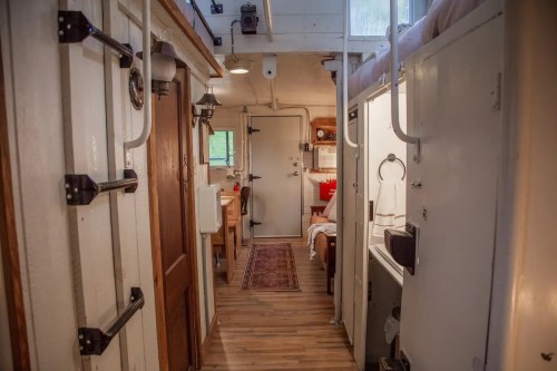Interior view of a cozy, narrow space with wooden floors, a dining area, and compact sleeping and bathroom areas.