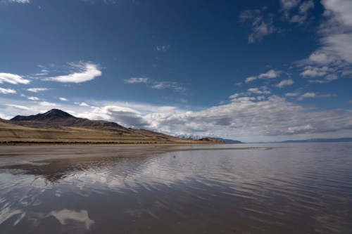 A serene landscape featuring a calm lake reflecting clouds and mountains under a blue sky.