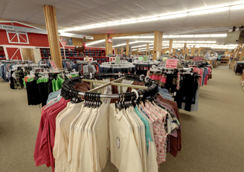 A spacious retail store interior filled with clothing racks and a circular display of shirts in the foreground.