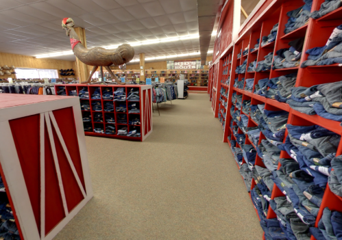 A spacious store aisle lined with shelves of jeans and a large decorative rooster statue in the background.