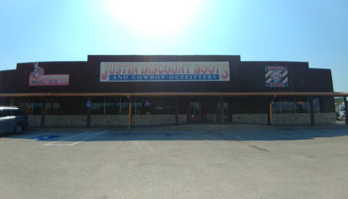 Exterior of Justin Discount Boots and Cowboy Outfitters store, featuring a large sign and clear blue sky.