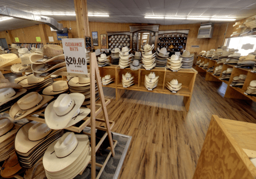 A spacious store interior filled with rows of cowboy hats on display, with a clearance sign for $20 hats.