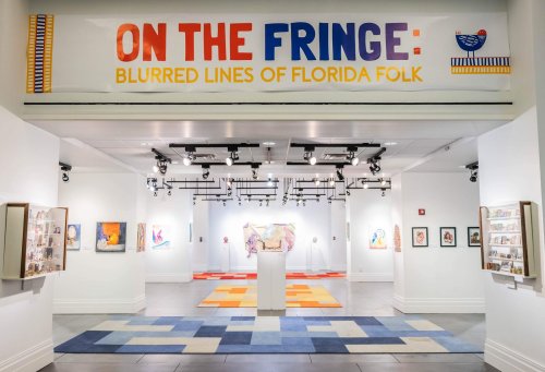 Art gallery interior featuring the exhibit "On the Fringe: Blurred Lines of Florida Folk" with colorful artwork and displays.