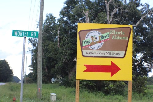 Sign for Yogi Bear's Camp-Resort in Elberta, Alabama, with a directional arrow and nearby road sign for Wortel Rd.