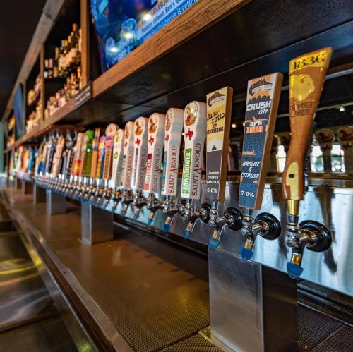 A row of colorful beer taps with various labels and styles in a bar setting.
