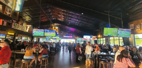 A lively sports bar filled with people, featuring multiple TVs showing games and a vibrant atmosphere.