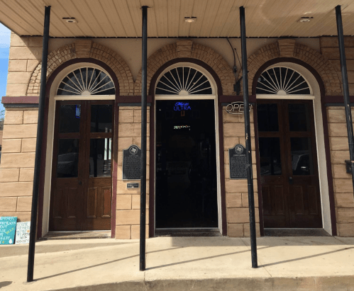 Exterior view of a building with three arched doorways, featuring wooden doors and a sign indicating it's open.