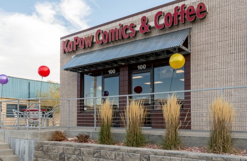 Exterior of KaPow Comics & Coffee, featuring a sign, colorful balloons, and decorative plants in front.