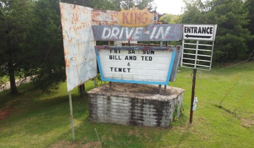 A weathered drive-in movie marquee displaying "Fri, Sat, Sun: Bill and Ted & Tenet" with an entrance sign nearby.