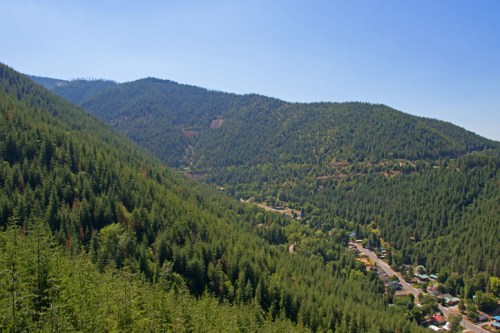 A panoramic view of lush green mountains and valleys under a clear blue sky, with a small town visible below.