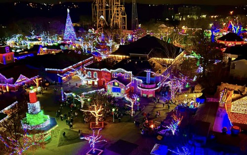 A vibrant holiday scene featuring a theme park adorned with colorful lights, a decorated tree, and festive decorations.