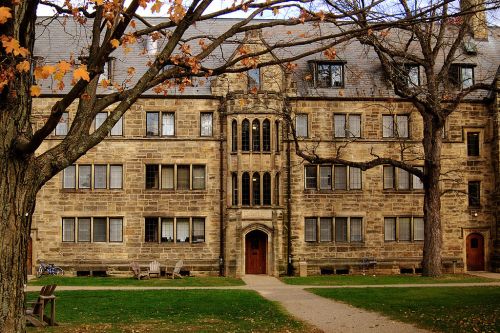 Historic stone building with large windows, surrounded by trees and autumn leaves, set in a grassy area.