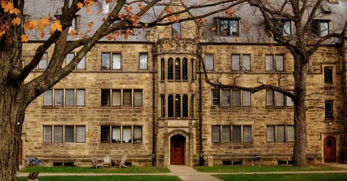 Historic stone building with large windows, surrounded by trees and a grassy area. Autumn leaves are visible.