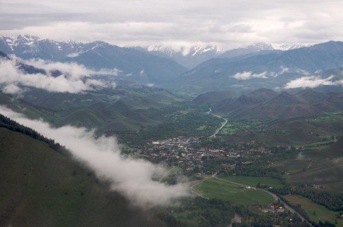 Aerial view of a valley surrounded by mountains, with a small town nestled among green fields and clouds.