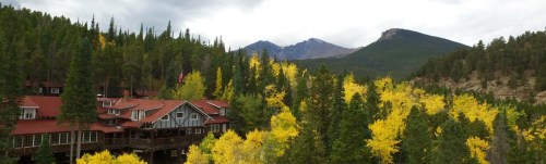 A scenic view of a lodge surrounded by vibrant yellow trees and mountains under a cloudy sky.