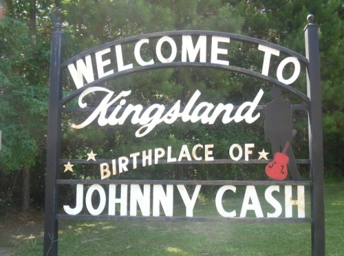 Sign welcoming visitors to Kingsland, birthplace of Johnny Cash, surrounded by greenery.