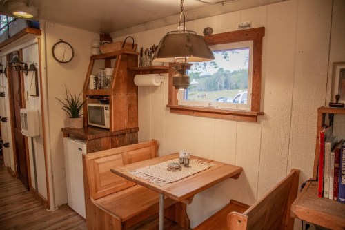Cozy kitchen nook with wooden table, benches, and shelves, featuring a microwave and decorative plants.