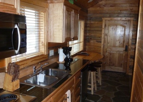Cozy wooden kitchen with a sink, microwave, and a small dining area featuring stools and a door to the outside.