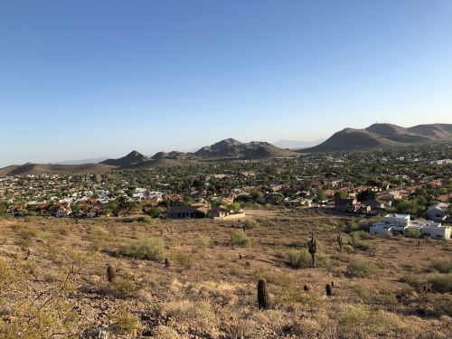 A panoramic view of a desert landscape with mountains in the background and a suburban area below.