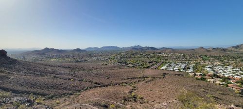 Panoramic view of a desert landscape with mountains in the distance and a residential area below. Clear blue sky.