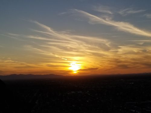 A vibrant sunset with orange and yellow hues, casting light over distant mountains and a sprawling landscape.