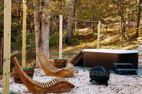 A serene outdoor space with wooden lounge chairs, a hot tub, and a fire pit surrounded by trees and string lights.