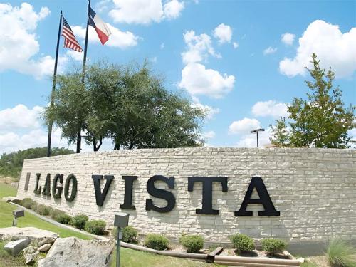 Sign for Lago Vista with American and Texas flags in the background, surrounded by greenery and blue skies.